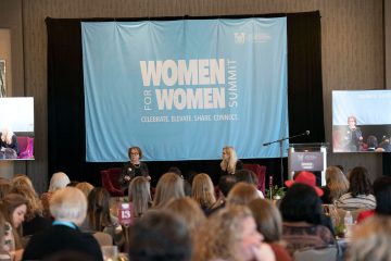 Wide shot of speakers on stage and attendees in audience at the Women for Women Summit presented by the College of Charleston School of Business